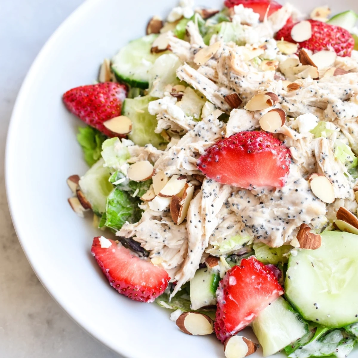 Served chilled on a white platter, Strawberry Poppy Seed Chicken Salad features feta crumbles and vibrant red onion slices.