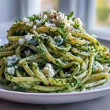 Plate of Linguine with Arugula Pesto garnished with extra Parmesan and cracked black pepper, served on a rustic table.