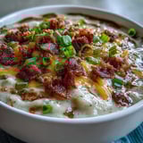 Bowl of velvety loaded potato soup garnished with sharp cheddar cheese, sour cream, and diced jalapeños for extra heat.