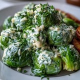 Brussels sprouts in Cream Cheese-Mustard Sauce plated alongside sliced chicken breast for a hearty dinner.