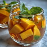 Refreshing non-alcoholic sangria with ripe mango, peach, and citrus, served over ice with a sprig of mint for garnish.
