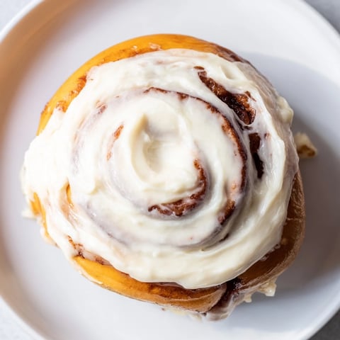 Freshly baked Pumpkin Cinnamon Rolls with soft, pillowy dough, a sweet cinnamon swirl, and creamy frosting on a rustic table.  