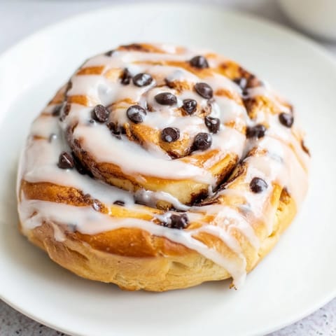 Golden-brown Nutella Chocolate Chip Rolls in a baking pan, glistening with a sweet glaze and extra chocolate chips for a rich, indulgent treat.