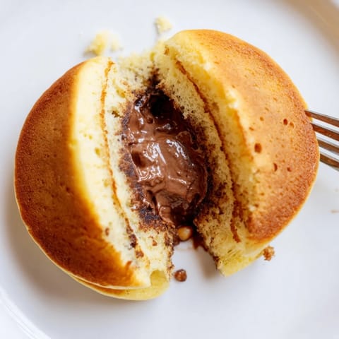 Golden-brown Nutella Stuffed Pancakes served warm with sliced strawberries and a drizzle of extra chocolate hazelnut spread.  