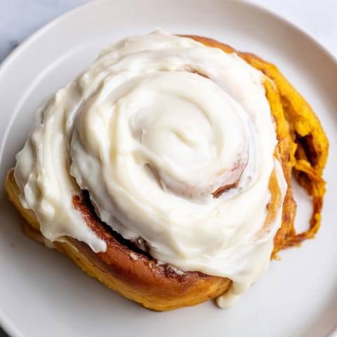 Golden brown Pumpkin Cinnamon Rolls topped with luscious cream cheese frosting, served warm on a cozy autumn morning.  
