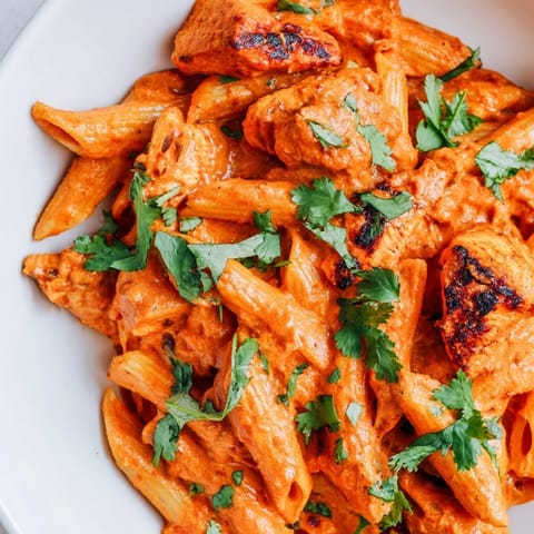 A close-up of Chicken Tikka Pasta reveals tender chicken tikka nestled in a vibrant, creamy tomato sauce clinging to al dente penne.