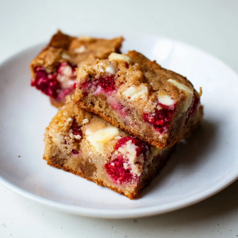 A close-up of freshly baked decadent white chocolate and raspberry blondies, showcasing gooey texture and bright fruit.