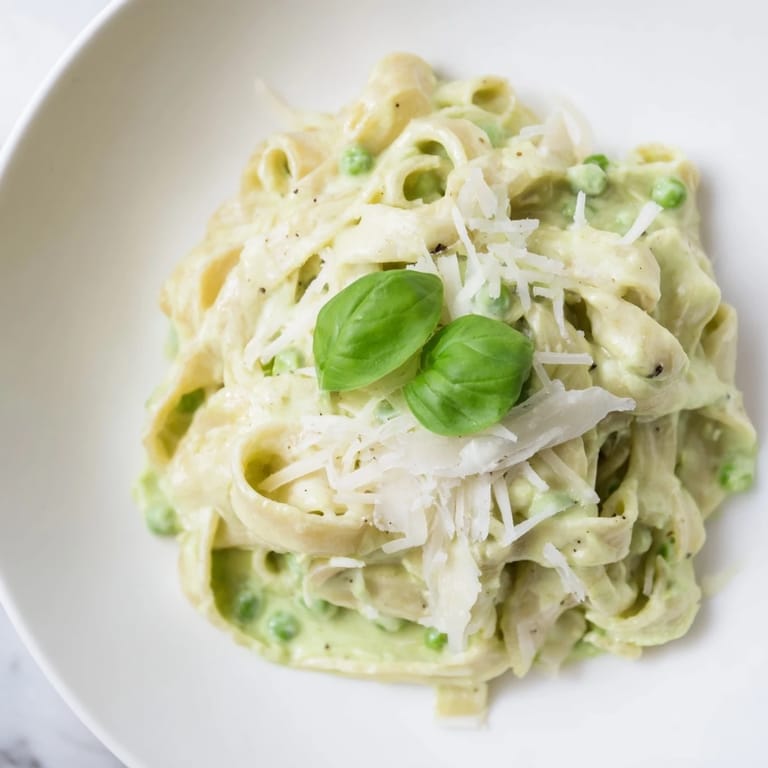 Plated Creamy Green Pea Alfredo pasta with a rich, velvety sauce and a squeeze of lemon.