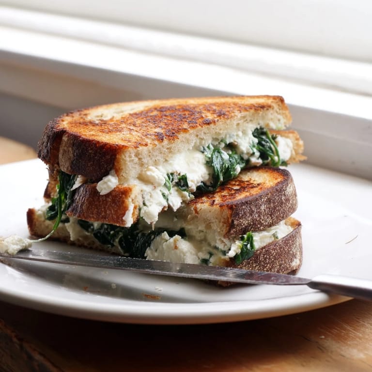This vegetarian Feta & Spinach Stuffed Grilled Cheese is sliced to reveal the vibrant, flavorful interior.